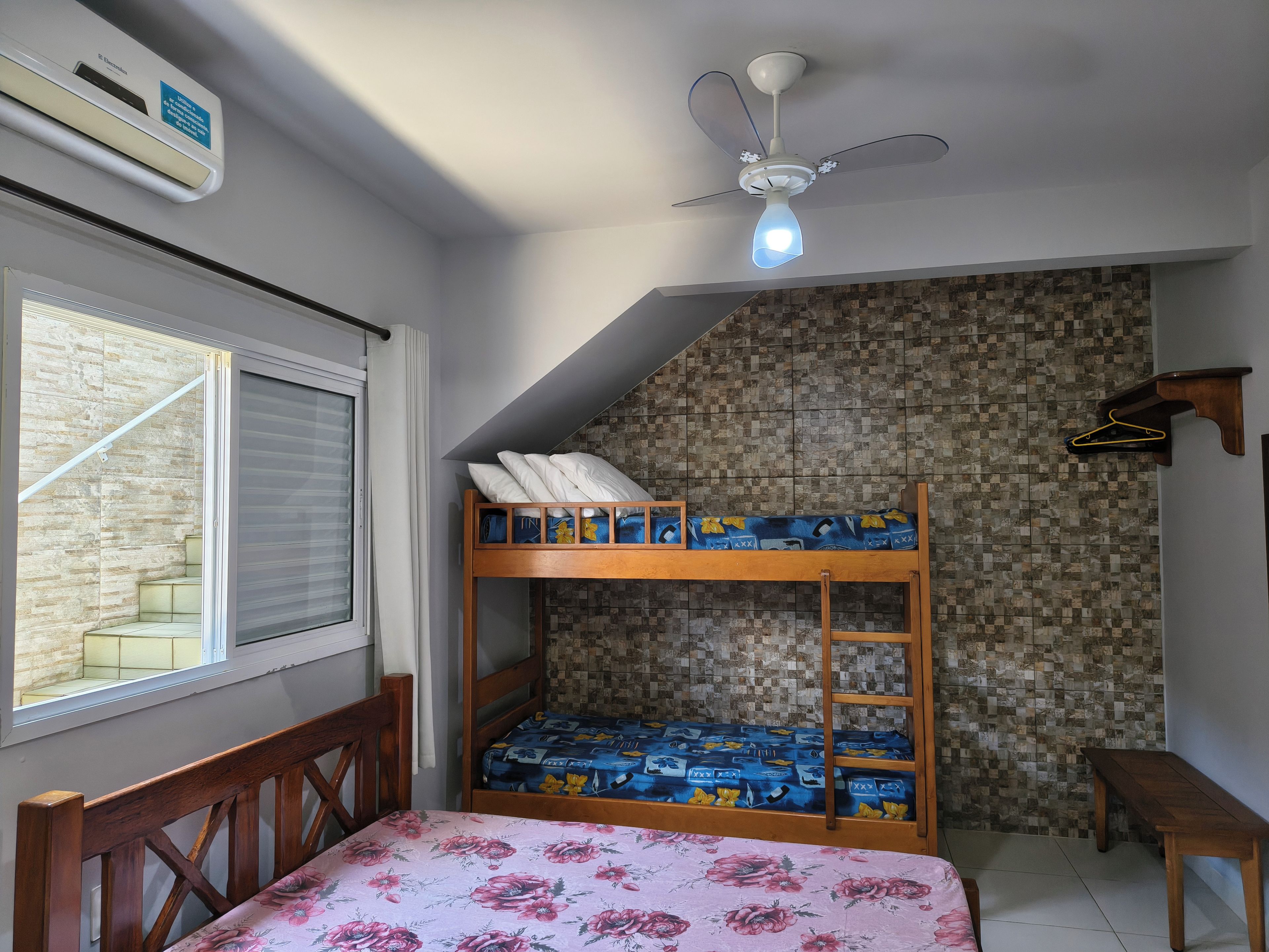 A room with a bunk bed, a desk, a chair, a hanging coat rack, and a window with blinds.