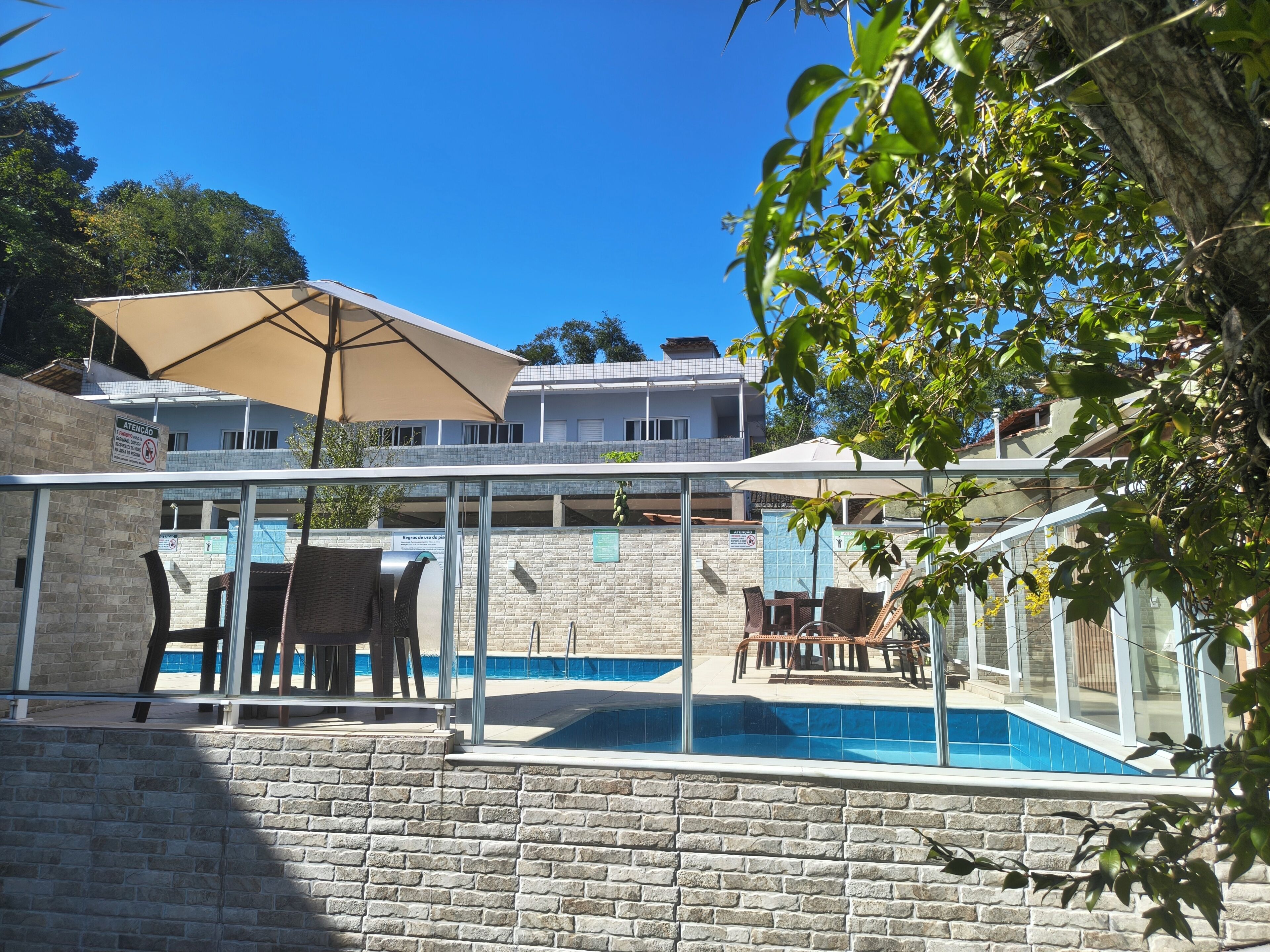 Une piscine dotée d’une enceinte en verre, entourée de murs en pierre, et un espace patio aménagé avec du mobilier d’extérieur.
