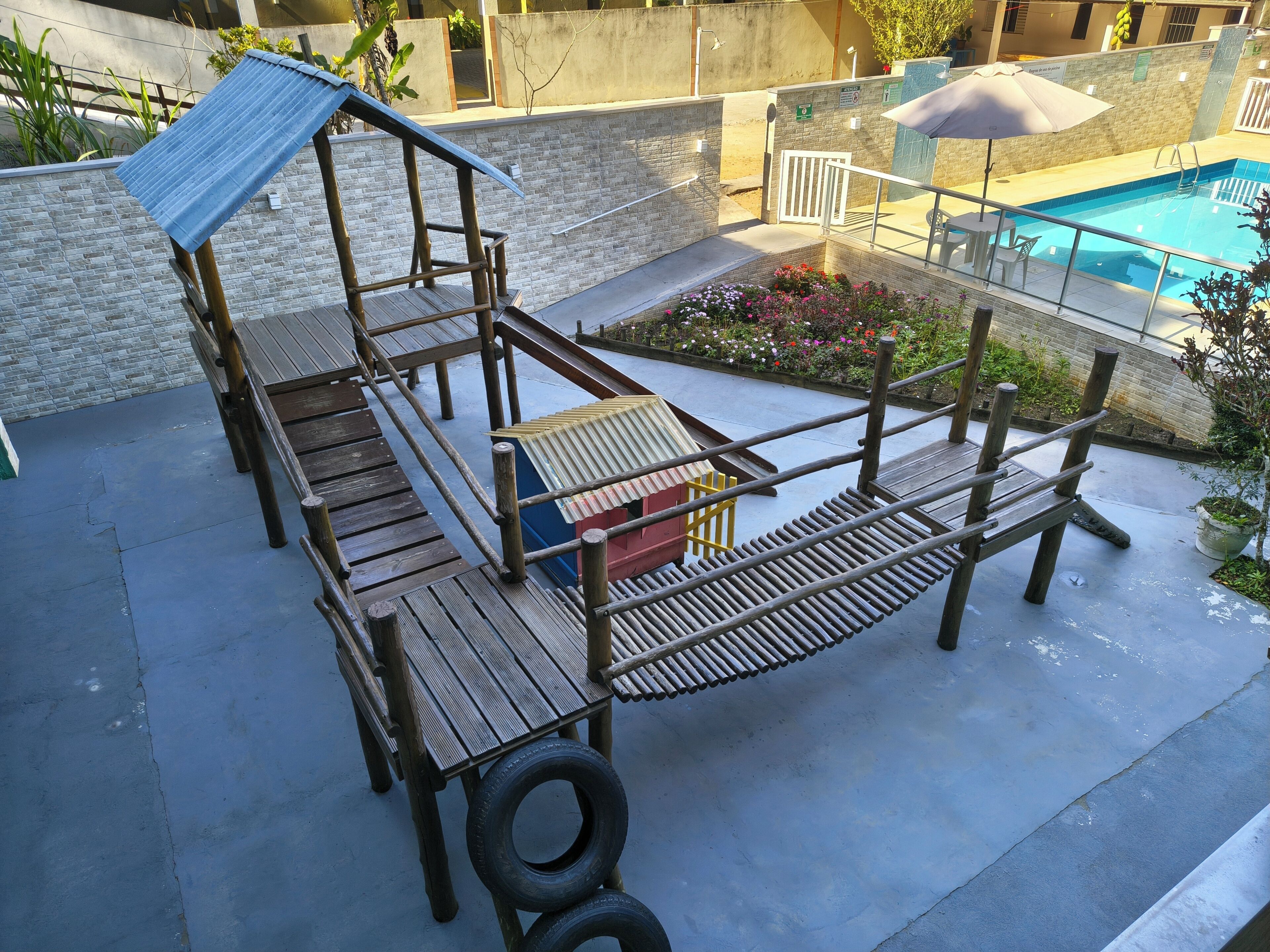 A wooden deck with a play structure, a pool, and a seating area with an umbrella.