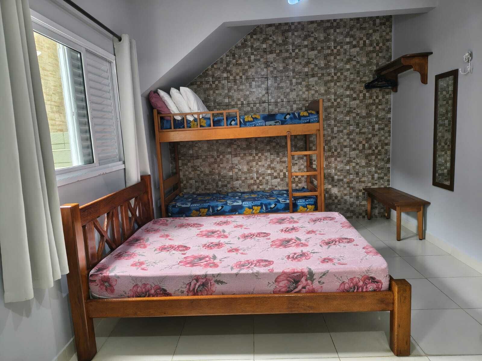 Un lit superposé avec une couvre-lit à motifs floraux, un banc en bois et un mur recouvert de carreaux.