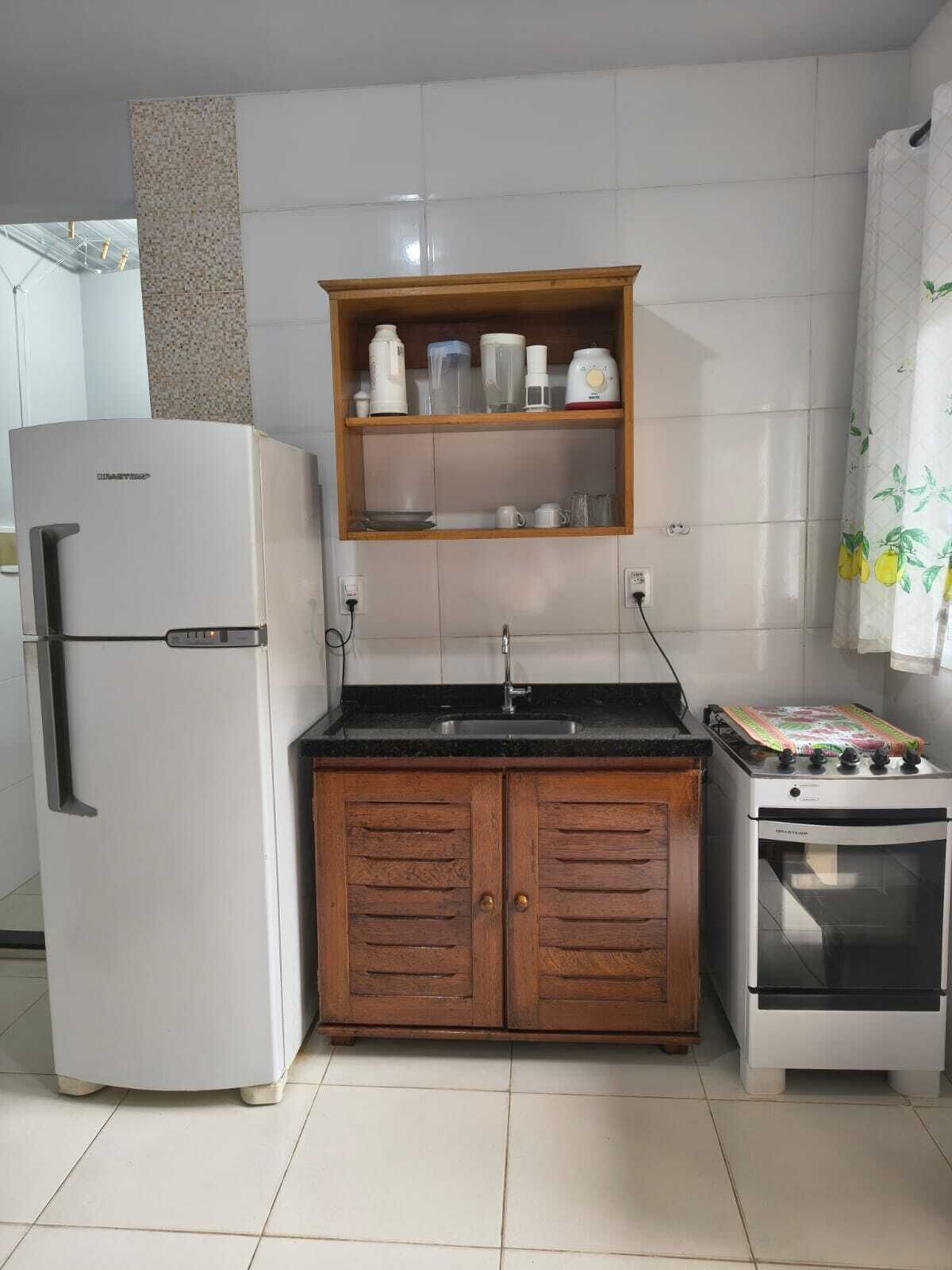 Een kleine keuken met een koelkast, een houten kast, een spoelbak en een oven.