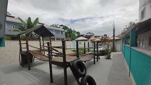 Ein Spielplatz mit Holzelementen und Reifen, ein Schwimmbecken und ein Gebäude mit blauer Fassade.