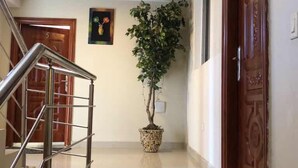 A hallway with a staircase, a potted plant, a wooden door, and a framed picture on the wall. - FRF Hotel (Cap-Haitien)