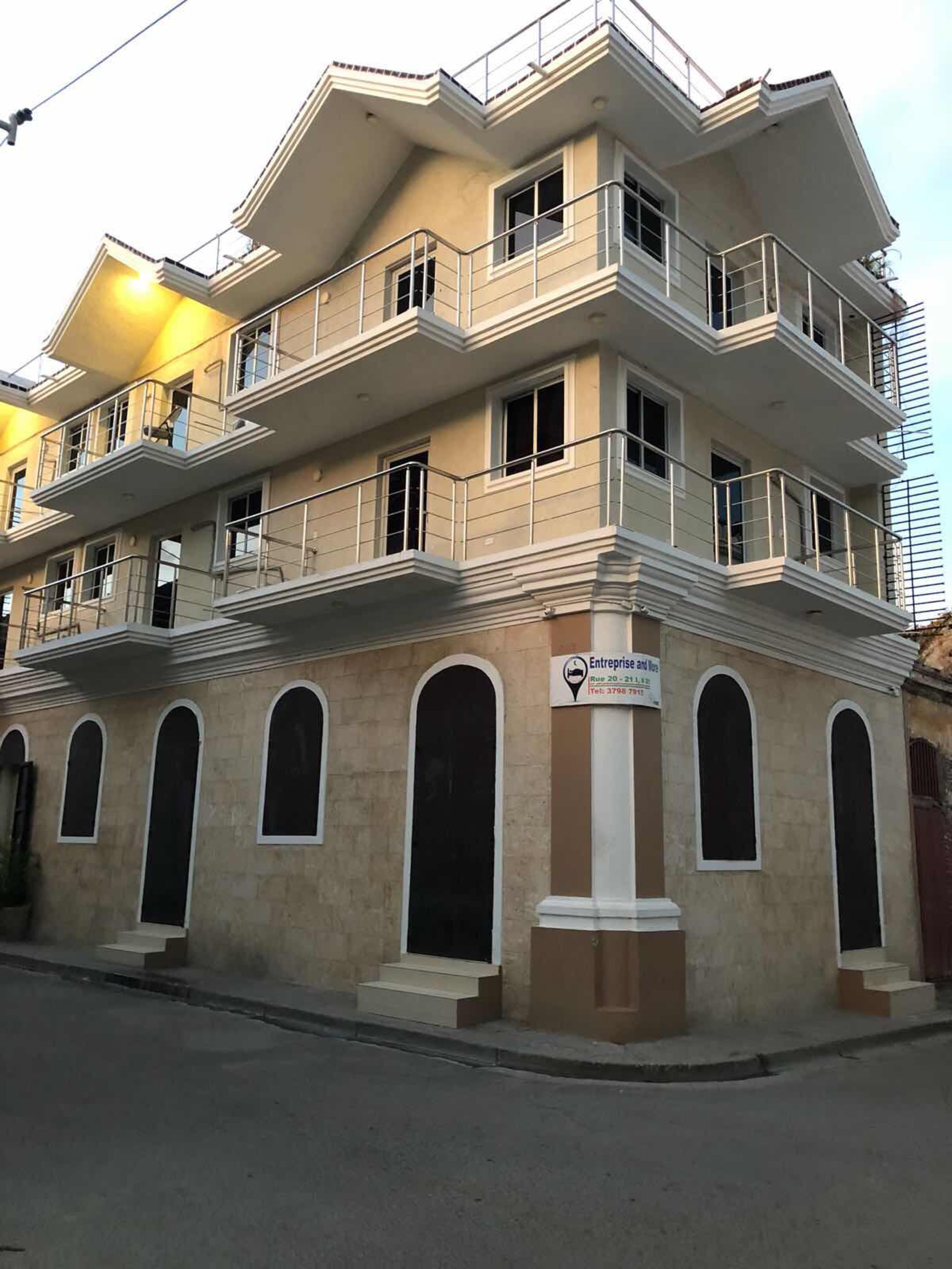 A multi-story building with balconies, a sign indicating it is an enterprise and house, and a street in front.