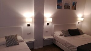 Une chambre d’hôtel avec deux lits, chacun étant équipé d’un oreiller et d’une table de chevet. Des lampes murales sont fixées au-dessus de chaque lit.