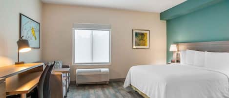 Une chambre d’hôtel équipée d’un lit, d’un bureau, d’une chaise, d’un climatiseur et ornée d’œuvres d’art sur les murs.