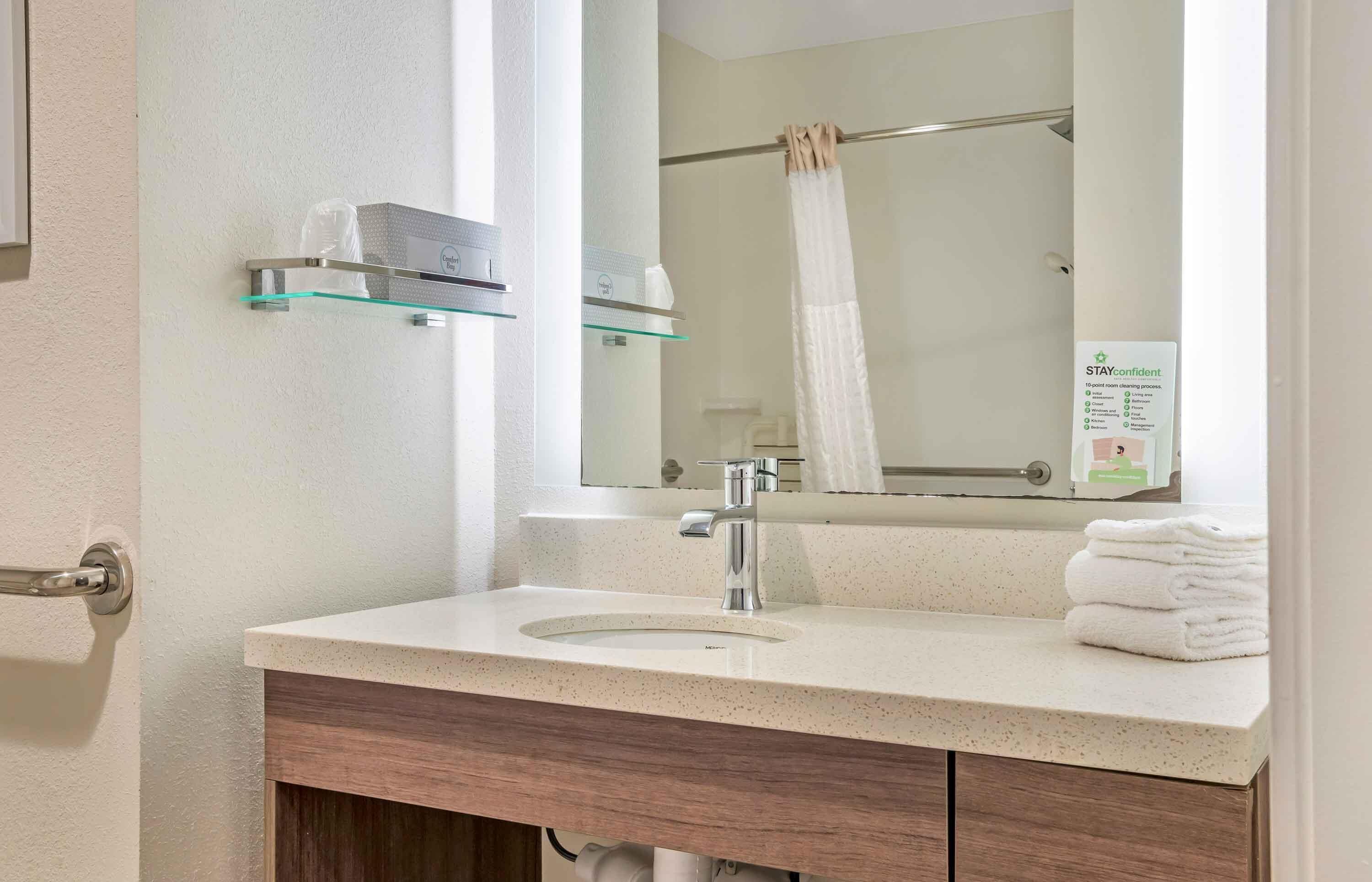 Ein Badezimmer mit Waschbecken, Spiegel, Handtuchhalter und einem Glastischchen.