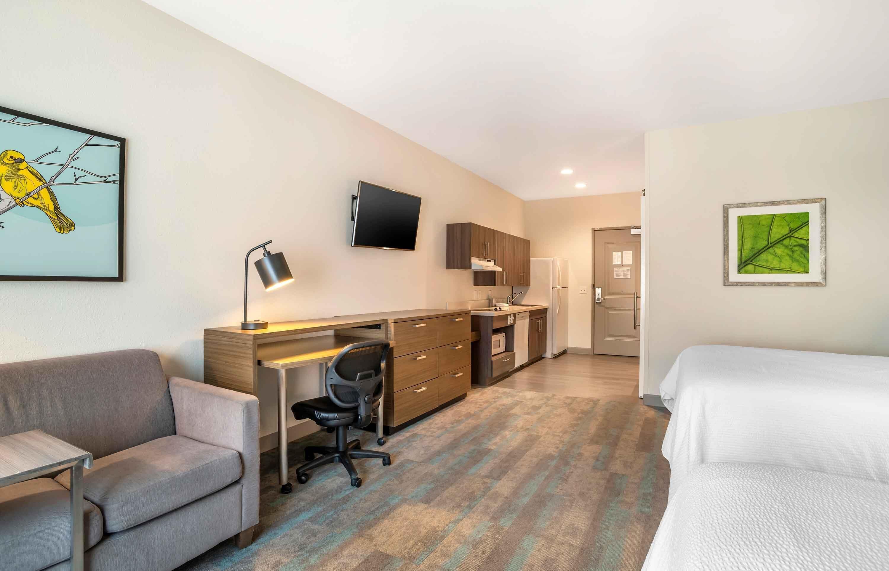 Een hotelkamer met een bank, een bureau met stoel, een bed, een flatscreen-televisie en een foto in een groene lijst aan de muur.