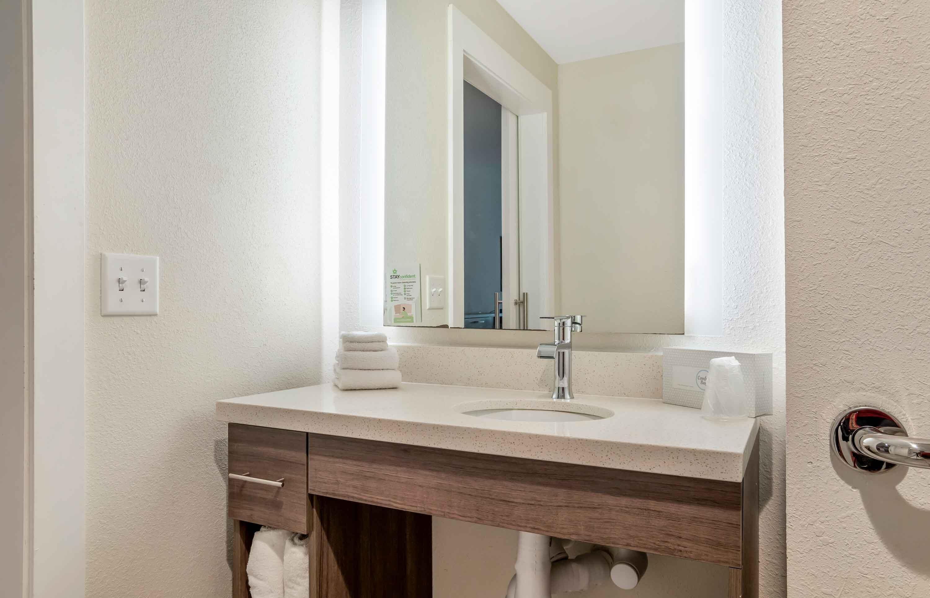 A bathroom with a sink, mirror, towel rack, and a towel dispenser.
