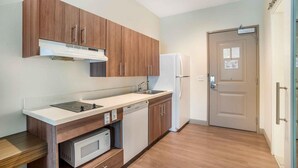 A compact kitchen with wooden cabinets, a built-in microwave, a dishwasher, and a refrigerator. - Extended Stay America Premier Suites Greenville Woodruff Rd (Greenville)