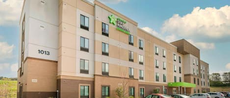 A hotel with a modern design, featuring a prominent logo, multiple windows, and a parking lot with several cars.