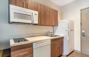 A modern kitchen with wooden cabinets, a white microwave, a stainless steel refrigerator, a dishwasher, and a sink. - Extended Stay America Premier Suites Greenville Woodruff Rd (Greenville)