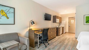 A hotel room with a desk, chair, bed, kitchenette, and a television. - Extended Stay America Premier Suites Greenville Woodruff Rd (Greenville)