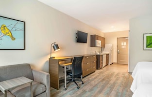Habitación de hotel con escritorio, silla, cama, kitchenette y televisión.