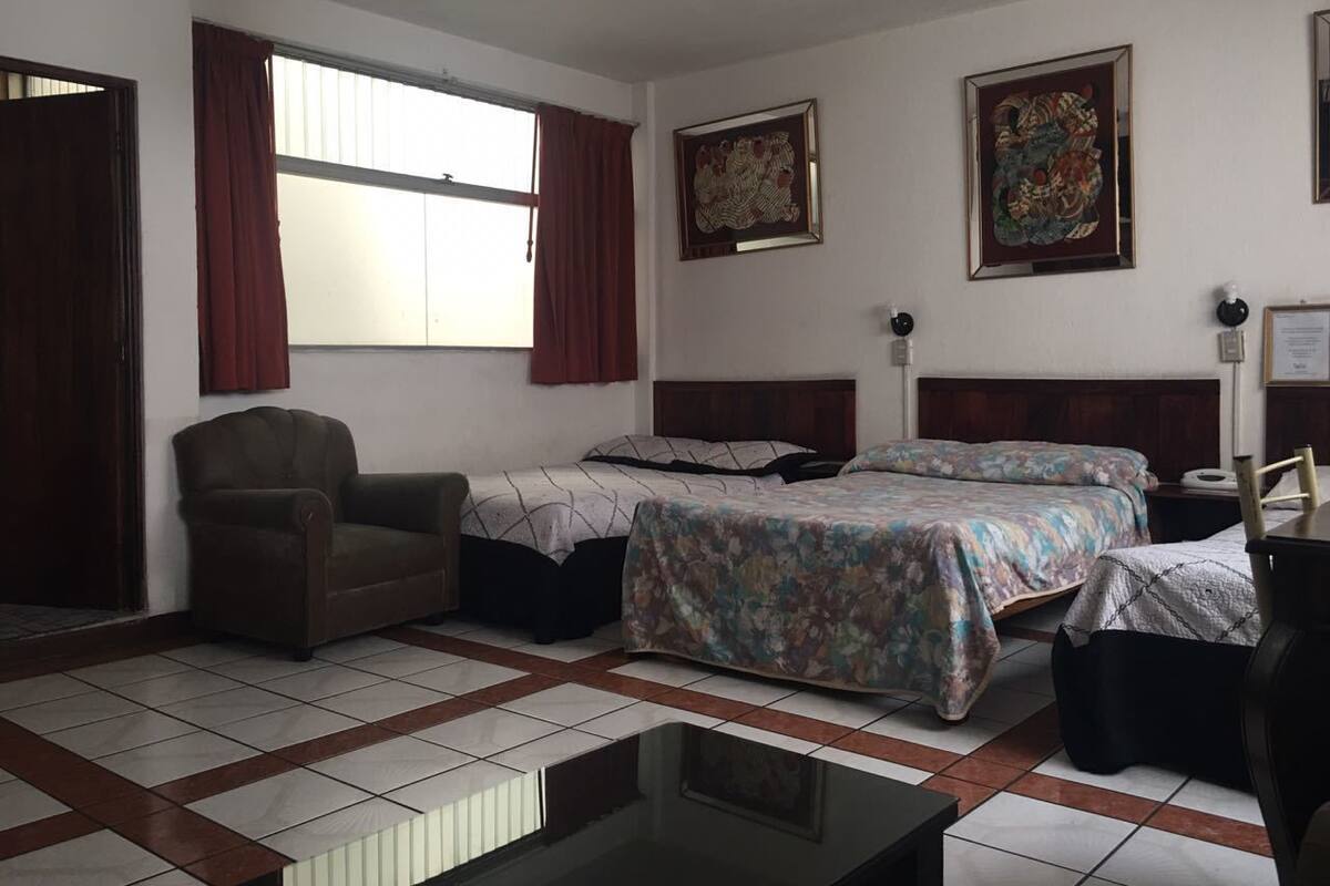 A hotel room with two beds, a chair, a table, and a window with curtains.