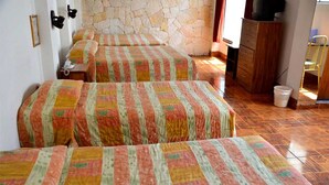 Una habitación con tres camas, una pared de piedra, un aparador de madera y un televisor encima.