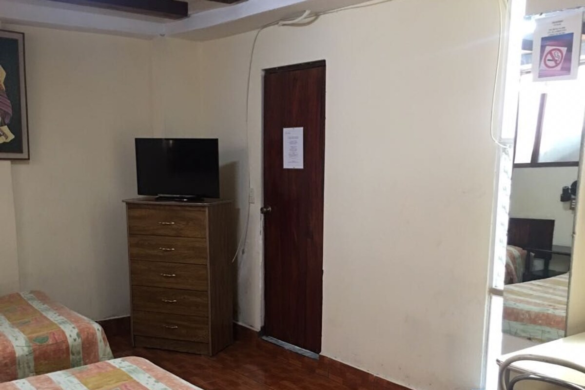 Een slaapkamer met twee bedden, een houten dressoir, een televisie en een deur met een bordje.