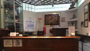 Mostrador de recepción de hotel con un calendario, una obra de arte enmarcada y un cartel que prohíbe fumar.