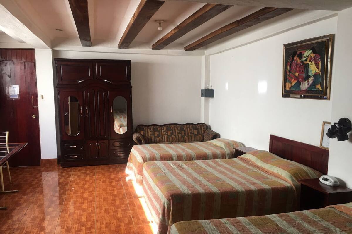 A hotel room with two beds, wooden flooring, a large wardrobe, and a painting on the wall.