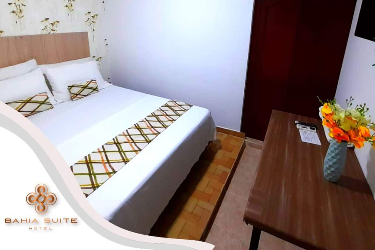 Ein Hotelzimmer mit Bett, Holz-Kopfteil, Nachttisch, Blumen in einer Vase und einem an der Wand montierten Fernseher.