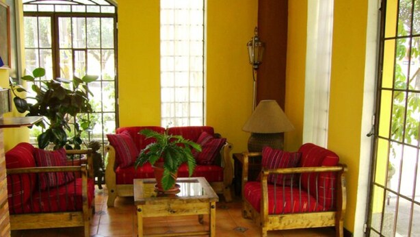A room with yellow walls, red sofas, a wooden coffee table, and a potted plant. - Eco Hotel Los Proceres (Guatemala City)