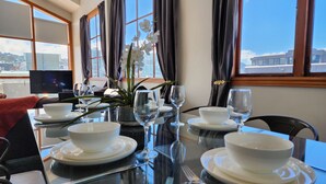 A dining table set with white plates, bowls, and wine glasses, with a vase of white flowers and a television in the background. - U Suites on Courtenay (Wellington)