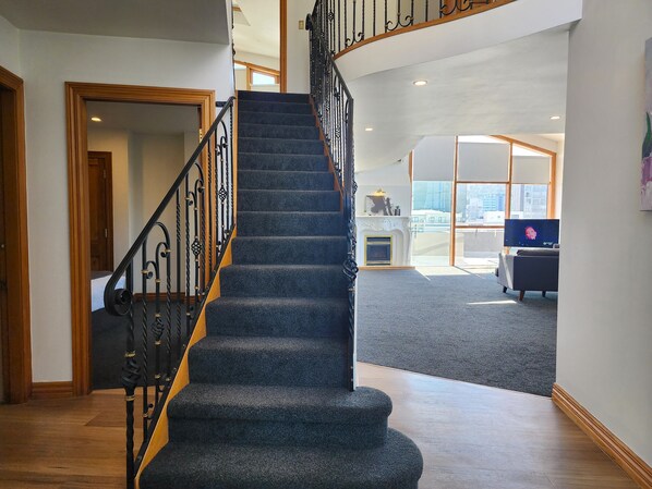 A staircase with black railings and carpeted steps leading to a living area with a fireplace and a television.