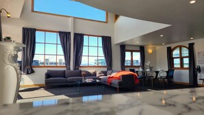 A spacious living room with a large window, a sofa, a coffee table, and a dining area. - U Suites on Courtenay (Wellington)