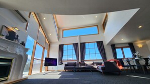 A spacious living room with a fireplace, a television, and a large window offering a view of the sky. - U Suites on Courtenay (Wellington)