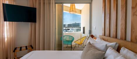 A hotel room with a bed, a TV, a balcony with a chair, and a view of the city.
