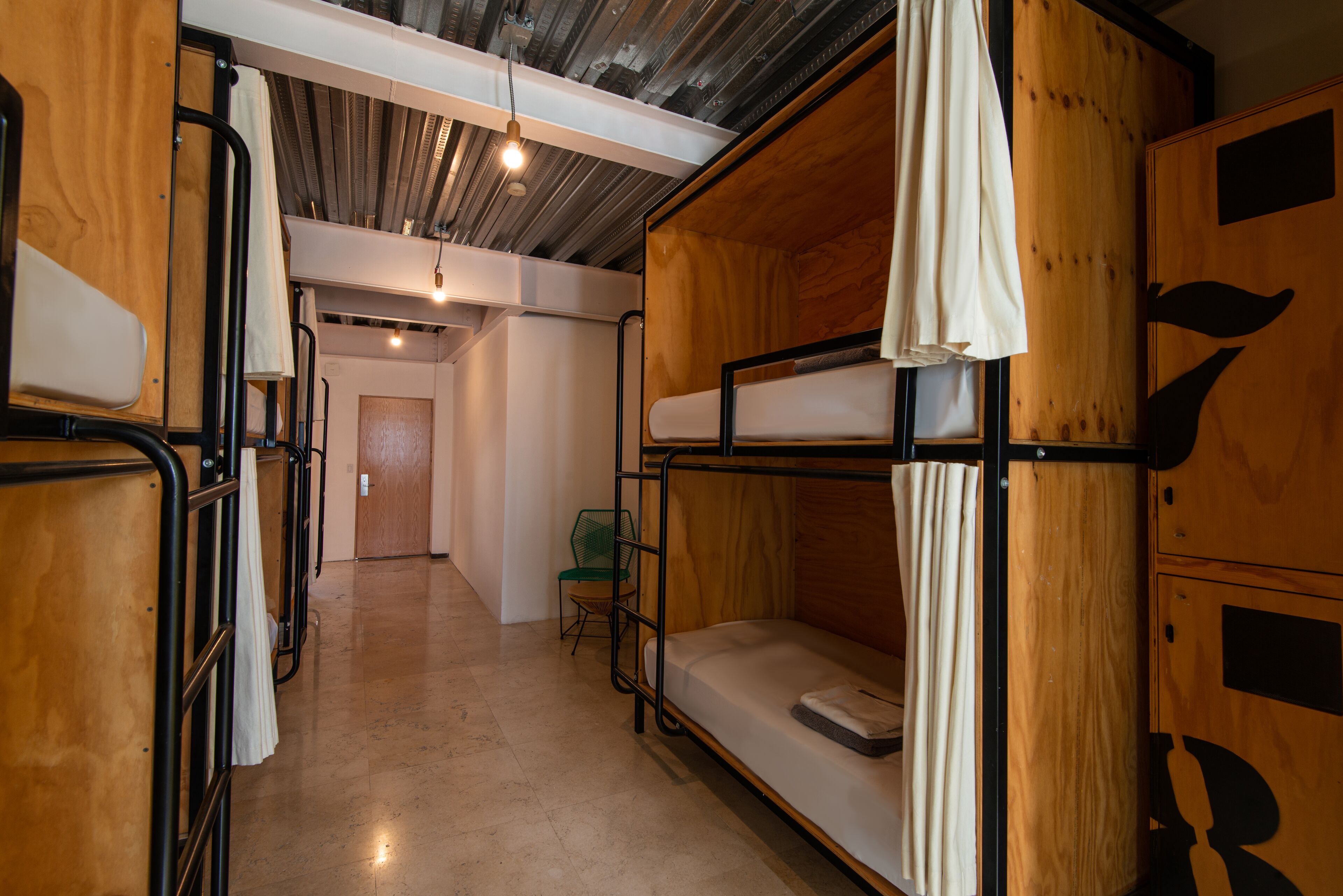 A bunk bed room with wooden walls and a metal frame, a small green chair, and a door in the background.