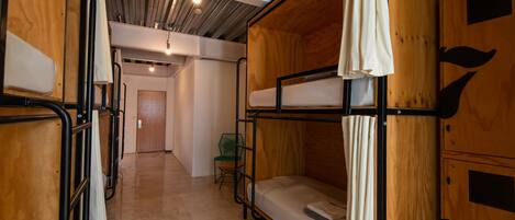 A bunk bed room with wooden walls and a metal frame, a small green chair, and a door in the background.
