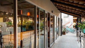 A covered outdoor area with glass doors leading to a restaurant, potted plants, and bicycles.