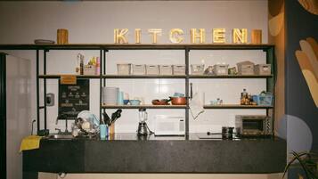 Un coin cuisine avec une enseigne indiquant « CUISINE » au-dessus d’un comptoir. On y trouve des étagères remplies de divers ustensiles de cuisine et un four à micro-ondes posé sur le comptoir.