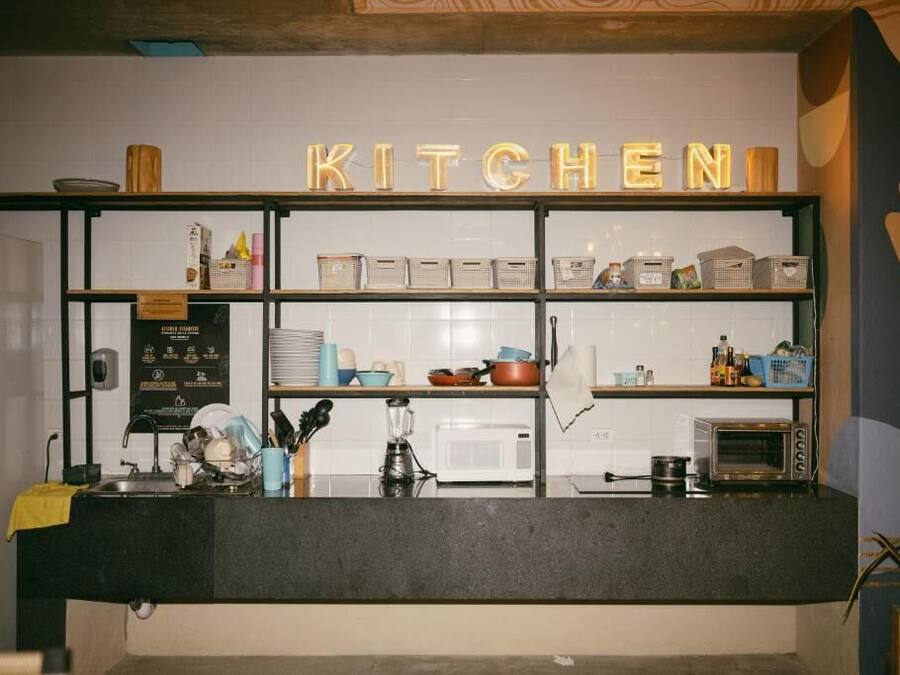 Un coin cuisine avec une enseigne indiquant « CUISINE » au-dessus d’un comptoir. On y trouve des étagères remplies de divers ustensiles de cuisine et un four à micro-ondes posé sur le comptoir.