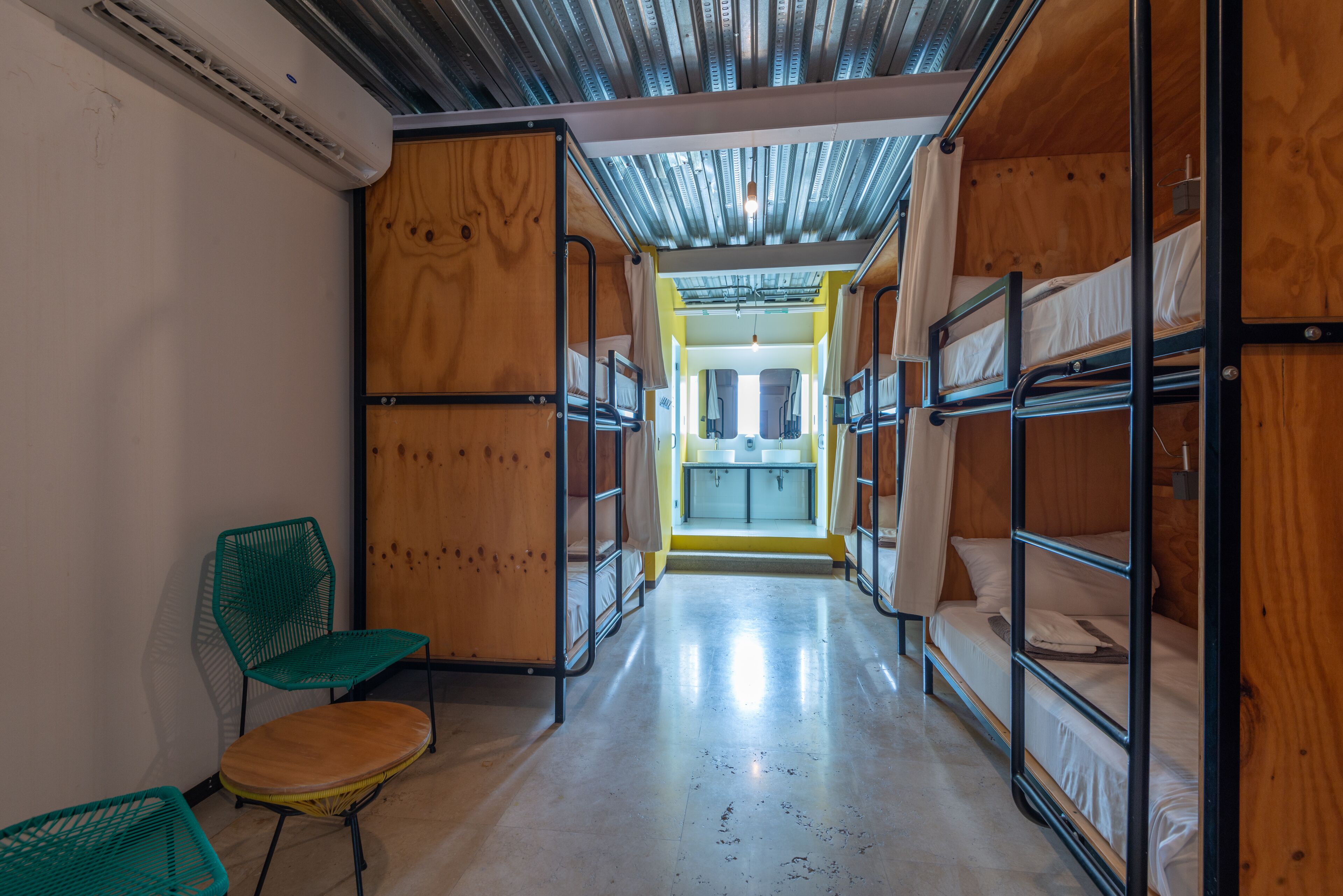 A corridor with bunk beds, a green chair, and a visible bathroom with a sink.