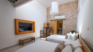 A modern hotel room with two beds, a TV, a bench, and a brick wall. - Mayan Monkey Los Cabos | Social Hotel (Cabo San Lucas)