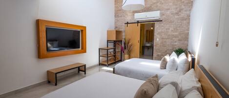 A modern hotel room with two beds, a TV, a bench, and a brick wall.