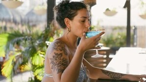 A person seated at a table with a drink, in an outdoor setting with a thatched roof and hanging baskets. - Mayan Monkey Los Cabos | Social Hotel (Cabo San Lucas)