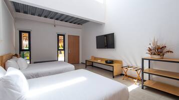 Habitació d'hotel moderna amb dos llits, una panxa de fusta, una televisió penjada a la paret i una taula petita amb un ram de flors seques.
