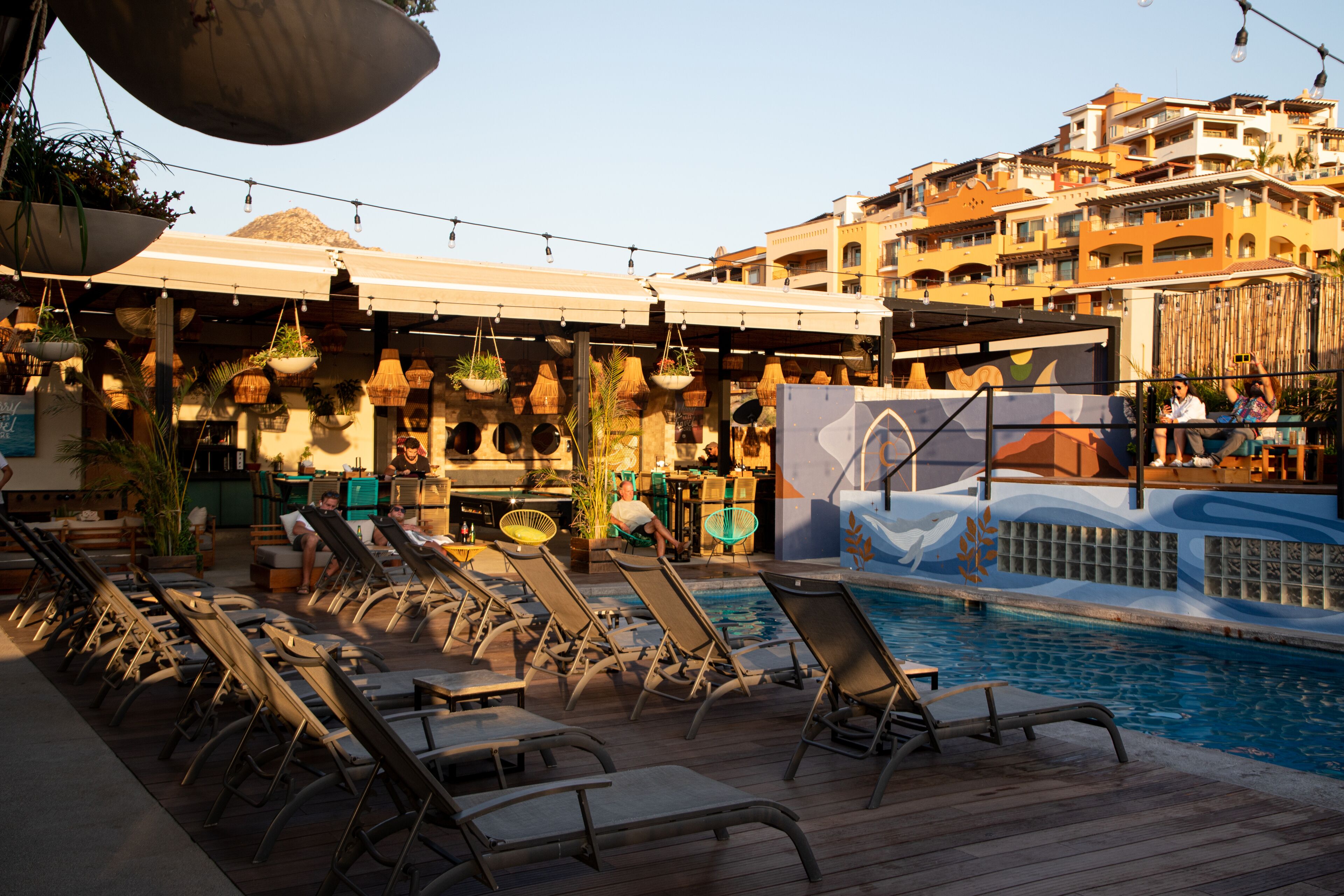 Un espace aménagé au bord de la piscine, avec des chaises longues, un bar et une vue sur le paysage urbain.