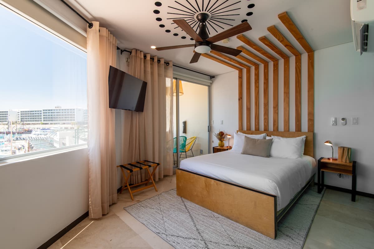 Una habitación de hotel moderna con una cama grande, un ventilador de techo, un televisor y vistas a la ciudad.