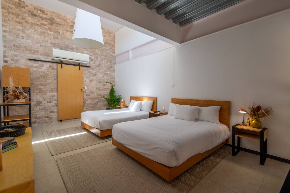 Un dormitorio moderno con dos camas, un armario de madera, una planta y una mesita con una lámpara.