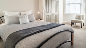 A bedroom with a bed, bedside table, lamp, chair, and a door with a window. - U Suites on Manners (Wellington)