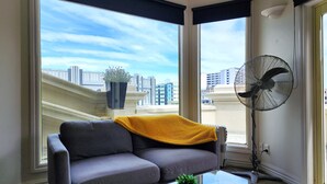 A modern living room with a grey sofa, a yellow throw blanket, a glass coffee table with a plant, and a standing fan. - U Suites on Manners (Wellington)