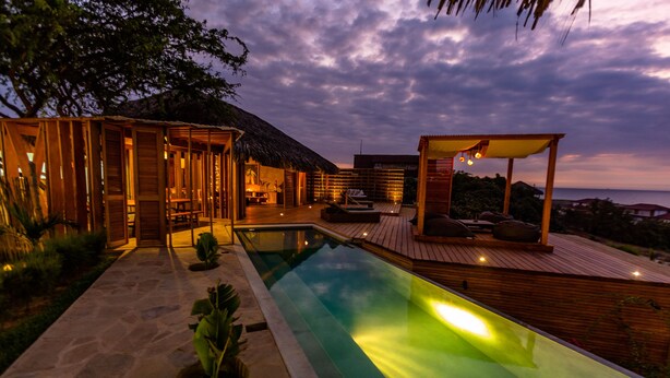 A modern resort with a swimming pool, wooden deck, and thatched-roof structures. - Casa Safran (Los Organos)