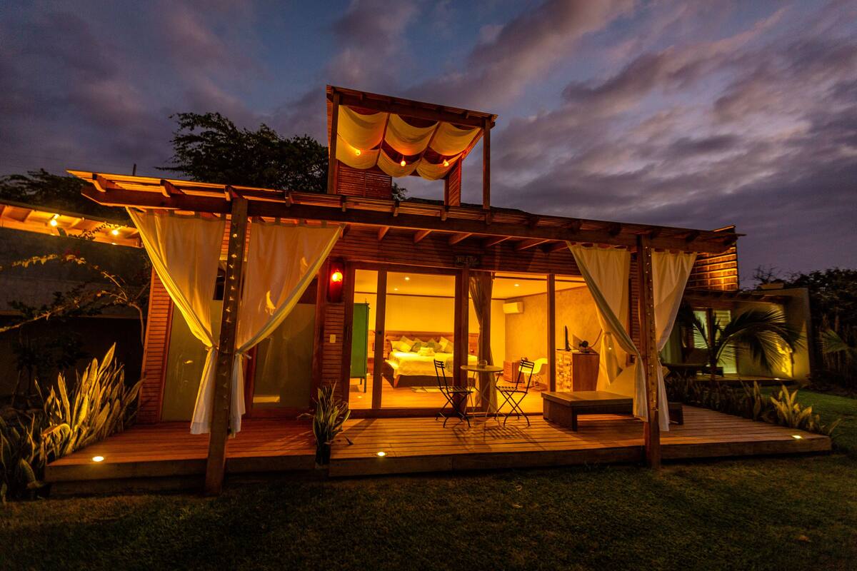 A modern outdoor bedroom with a wooden deck, a canopy, and a view of the surrounding garden.