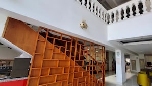 Un hall d’hôtel moderne avec un escalier en bois, un comptoir d’accueil et un espace salon doté de chaises jaunes.
