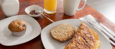 A breakfast setting with a muffin, toast, omelette, orange juice, coffee, and a teapot on a wooden table.