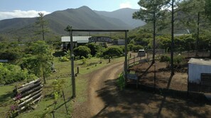 A rural landscape with a dirt road, a wooden fence, and a sign reading "Le Gîte du Koniambo". - Le Gite du Koniambo (Voh)